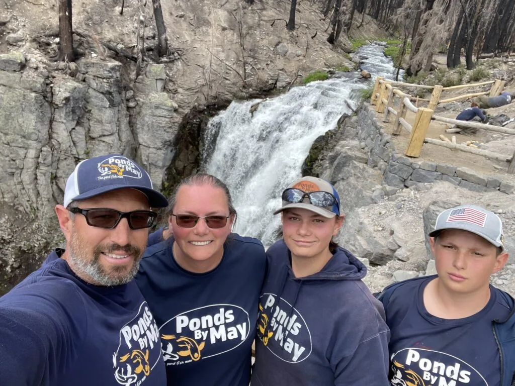 Four members of the Ponds By May crew in matching navy hoodies in front of a waterfall